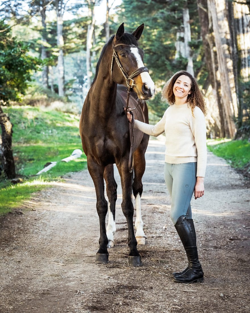 Sigourney Leigh Jellins standing with a bay horse on a tree-lined path