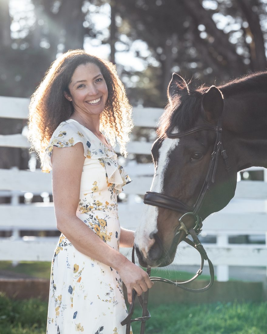Sigourney Leigh Jellins smiling beside a bay horse at a white fence
